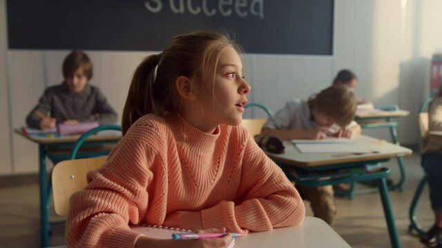 Thoughtful student sitting at school desk. Smiling girl answering questions