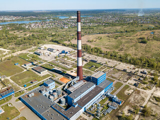 High chimney of a power plant on the outskirts of the city. Green spring steppe on the background. Aerial drone view.