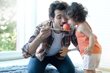 Father and little daughter with red apple, pretend eating their apple on  big wooden spoon, father...