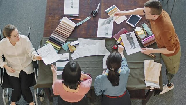 Top view time-lapse of diverse team of fashion designers working together on new collection. They are looking at sketches and choosing fabric