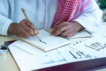 Arab men practicing writing Arabic ้with bamboo pens and ink on paper, Arabic letters mean the name of Muslim god 