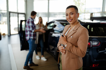 Smiling saleswoman holding a tablet while looking at camera at car showroom.