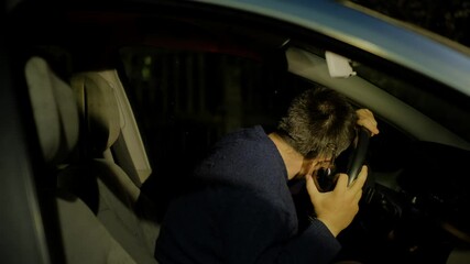 Drunk driver with empty alcohol bottle in hand puts head on steering wheel in car against flashing police lights at night closeup
