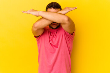 Young caucasian man isolated on yellow background keeping two arms crossed, denial concept.