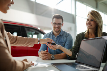 Female customer receiving car keys, shaking hands with saleswoman.
