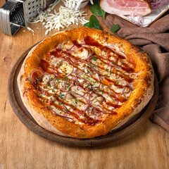 Delicious pizza with chicken fillet, ham, bacon, sausages, tomato sauce and mozzarella on wooden background.