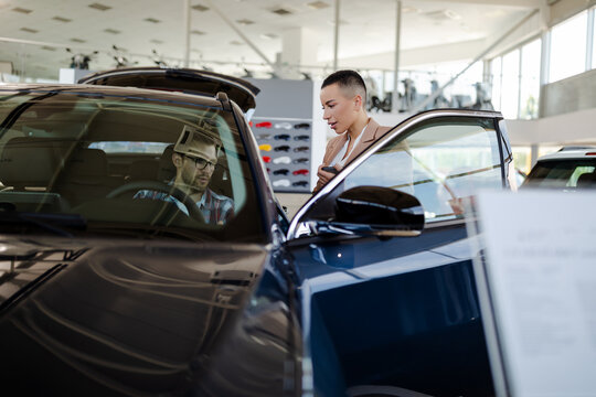 Test drive. Car buyer sitting in auto, choosing new automobile with seller In store.