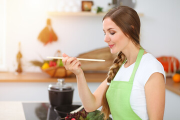 An attractive young woman preparing soup by new keto recipe while standing and smiling in sunny kitchen. Cooking and householding concepts