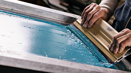 selective focus photo of male hands with squeegee. serigraphy production. printing images on...