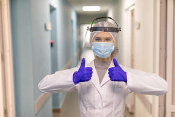 Fototapeta na wymiar Attractive female caucasian doctor in uniform and protective personal equipment smiling and showing two thumbs up.