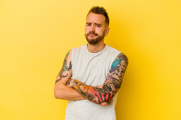 Young tattooed caucasian man isolated on yellow background suspicious, uncertain, examining you.
