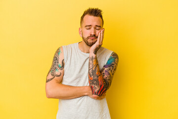 Young tattooed caucasian man isolated on yellow background who is bored, fatigued and need a relax day.