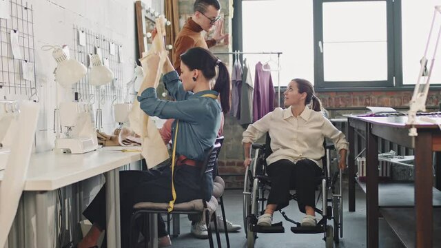 Slowmo shot of female fashion designer in wheelchair talking to her team working on new garments in studio
