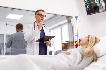 Obraz premium Mature doctor consulting patient lying on hospital bed talking happy about the diagnose and treatment in modern clinic background in health care and medical insurance concept