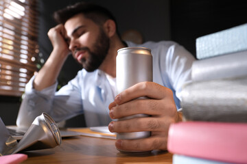 Tired young man with energy drink studying at home, focus on hand