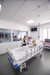 Mature doctor consulting patient lying on hospital bed talking happy about the diagnose and treatment in modern clinic background in health care and medical insurance concept