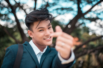 A young friendly asian man makes the finger heart gesture while at the park or school campus....