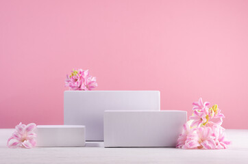 Spring gentle mockup with three white podiums for showing cosmetic product with hyacinth flowers and soft light pastel pink background.
