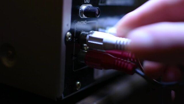 Male hand plugging RCA cables. Close-up. Red and White.