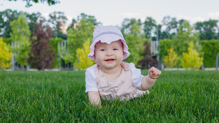 Cute 8 months old newborn nursing baby girl lying on the grass in the park and smiling on a summer sunny day. Place for text.