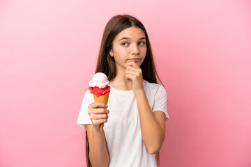 Little girl with a cornet ice cream over isolated pink background and looking up