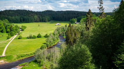 Quiet and green summer landscape with river, trees, houses, stones and summer sun, in Latvia by the Amata river and Zvārgzde rock