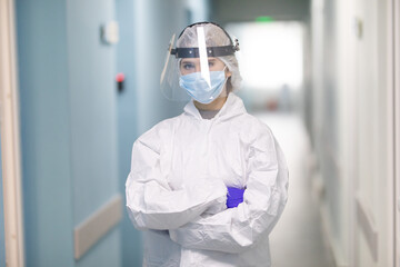 Fototapeta premium Young woman nurse adjusts her face shield at the hospital corridor during coronavirus pandemic. Healthcare, medicine and safely concept