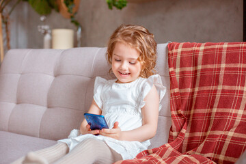 a little girl with a phone is sitting on the couch