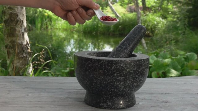 Hand is putting the rose peppercorns into the mortar in slow motion outdoors