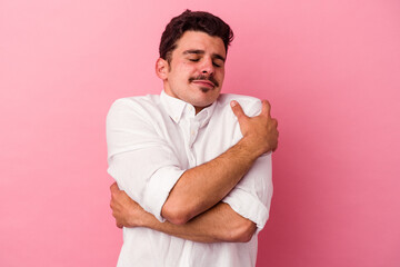 Young caucasian man isolated on pink background hugs, smiling carefree and happy.