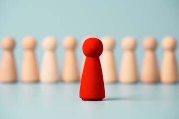 Red wooden figure standing in front of others figures on blue background, Leadership and management...