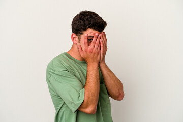 Young caucasian man isolated on white background blink through fingers frightened and nervous.