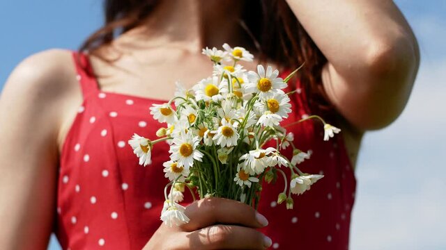 A woman in a red dress with polka dots holds a very beautiful bouquet of field daisies in her hands. 