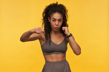 Confident beautiful african american young fitness woman doing shadow boxing exercises and looking at camera isolated over yellow background