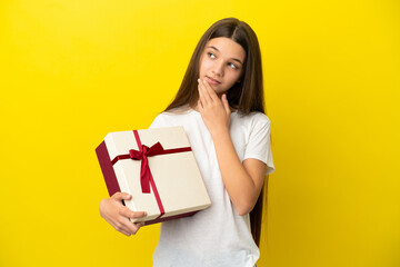 Little girl holding a gift over isolated yellow background looking up while smiling