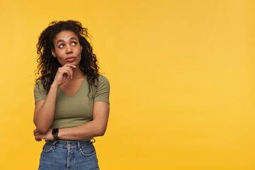 Pensive attractive african american young woman in casual clothes thinking and looking away to the side at copyspace isolated over yellow background Keep hands folded