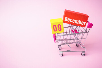December 9th. Day 9 of month, Calendar date. Close up toy metal shopping cart with red and yellow...