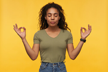 Calm pacified african american young woman in casual clothes keeps eyes closed and hands in mudra...