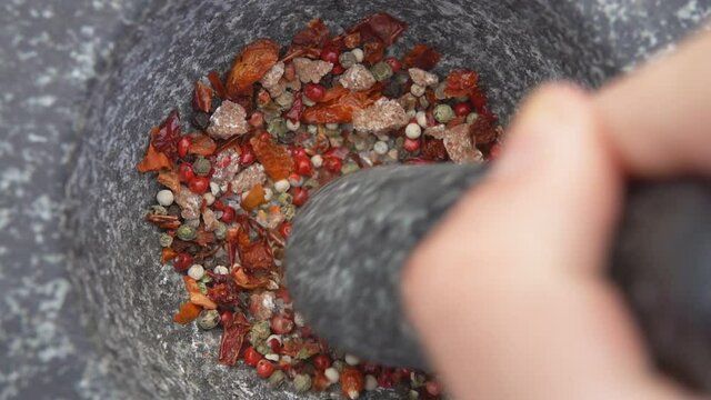 Hand with a pestle is grinding various kinds of spices in the grey stone mortar