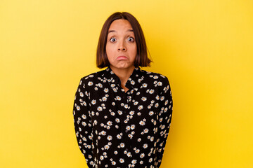 Young mixed race woman isolated on yellow background shrugs shoulders and open eyes confused.