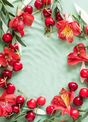 Cherry frame with red flowers and petals in water on natural green background