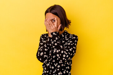 Young mixed race woman isolated on yellow background blink through fingers frightened and nervous.