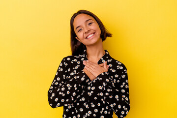 Young mixed race woman isolated on yellow background has friendly expression, pressing palm to chest. Love concept.