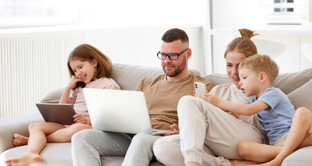Young family addicted with gadgets relaxing on sofa at home