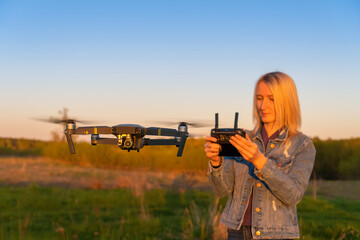 Young blonde woman controls a drone in nature during sunset. In the foreground is a close-up drone