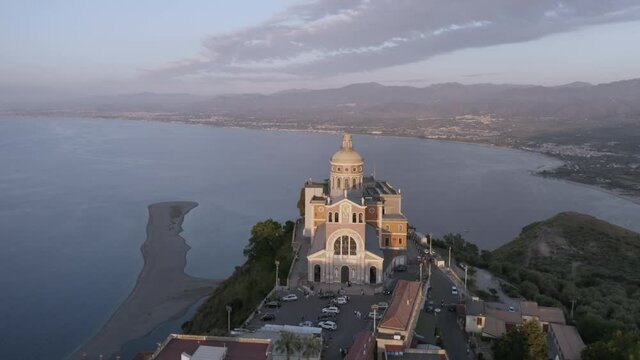 Panoramic Aerial still shot of Sanctuary of Tindari baroque facade from high angle view at sunset, iconic Sicily travel destinations in Italy. Beautiful christian baroque cathedral by the coastline