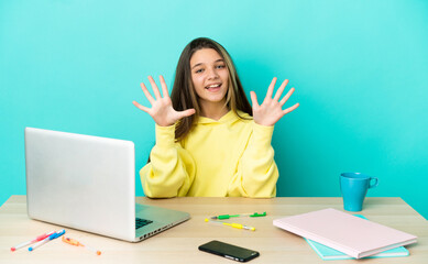 Little girl in a table with a laptop over isolated blue background counting ten with fingers