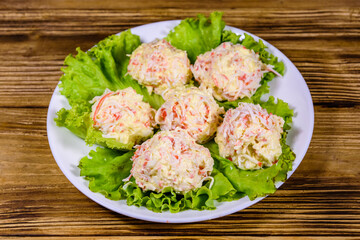 White plate with crab-cheese balls and lettuce leaves on wooden table