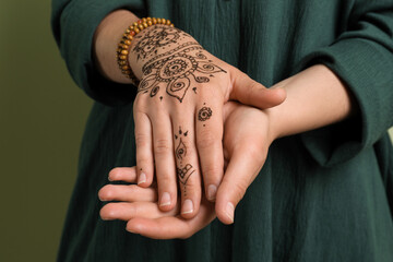 Woman with beautiful henna tattoo on hand against green background, closeup. Traditional mehndi