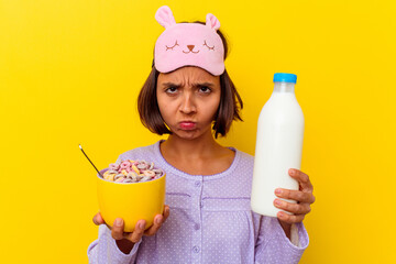 Young mixed race woman eating cereals wearing a pijama isolated on yellow background